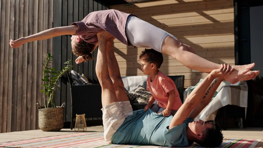 Father and kids doing yoga outdoors on a patio, balancing poses together.