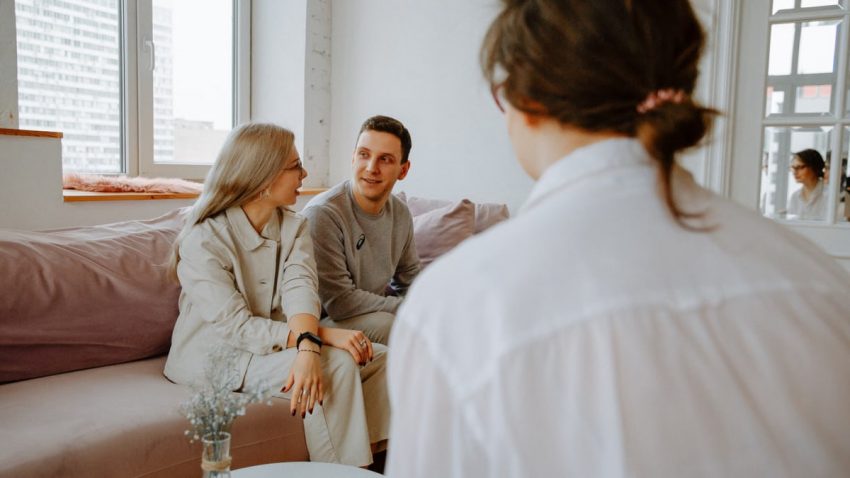 A couple engaged in a counseling session with a therapist in a modern indoor setting.